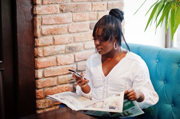 Stylish young black woman holding a newspaper and a phone